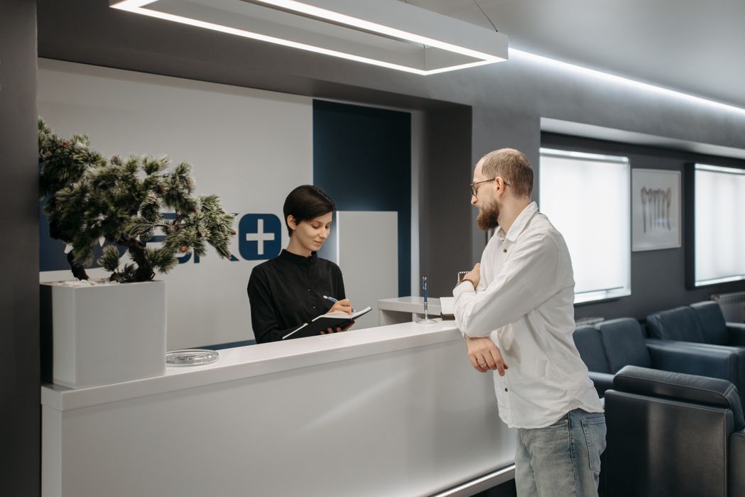 A man consults a receptionist in a modern clinic setting with contemporary design.
