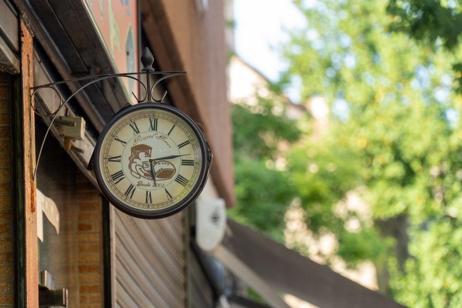 Charming vintage wall clock mounted on a building with blurred greenery background.